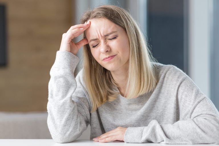 Femme aux cheveux blonds, main sur le front, souffrant de maux de tête ou de migraines