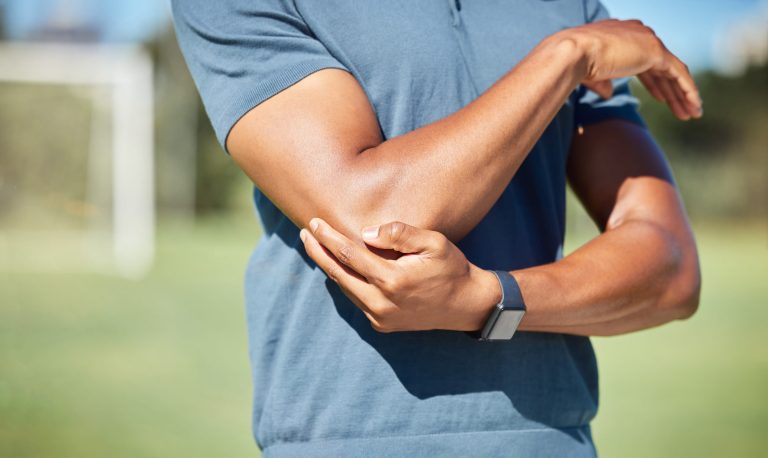 Personne tenant son coude avec la main opposée, suggérant une douleur ou une inflammation.